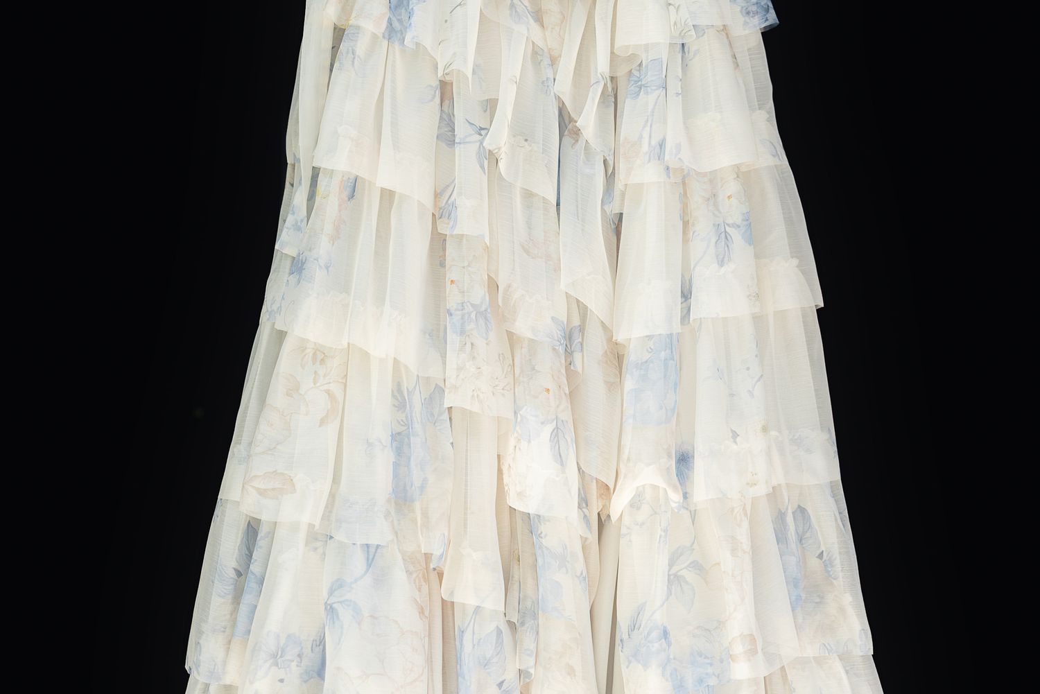 Elegant white tiered ruffle maxi skirt with delicate blue floral print, photographed against black background.