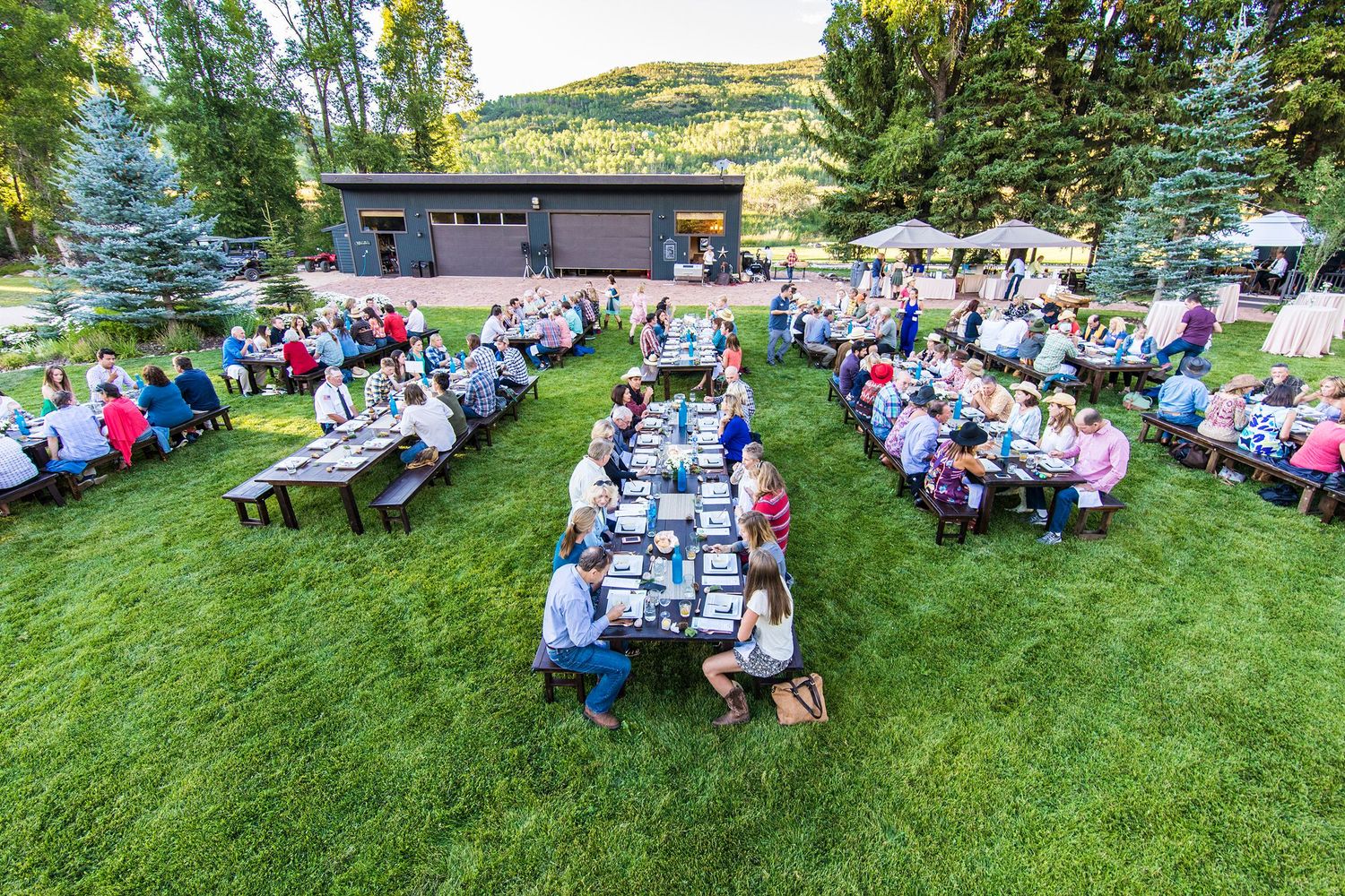Aerial view of outdoor event with guests seated at picnic tables on green lawn.