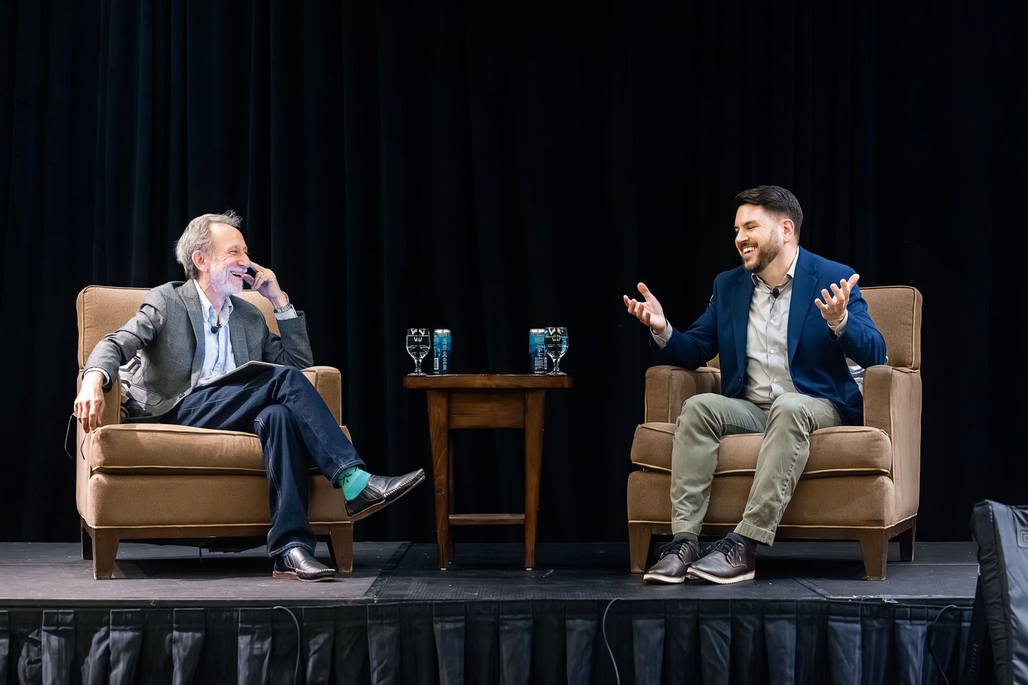 Two speakers engaged in conversation sitting in armchairs on a stage with black backdrop.