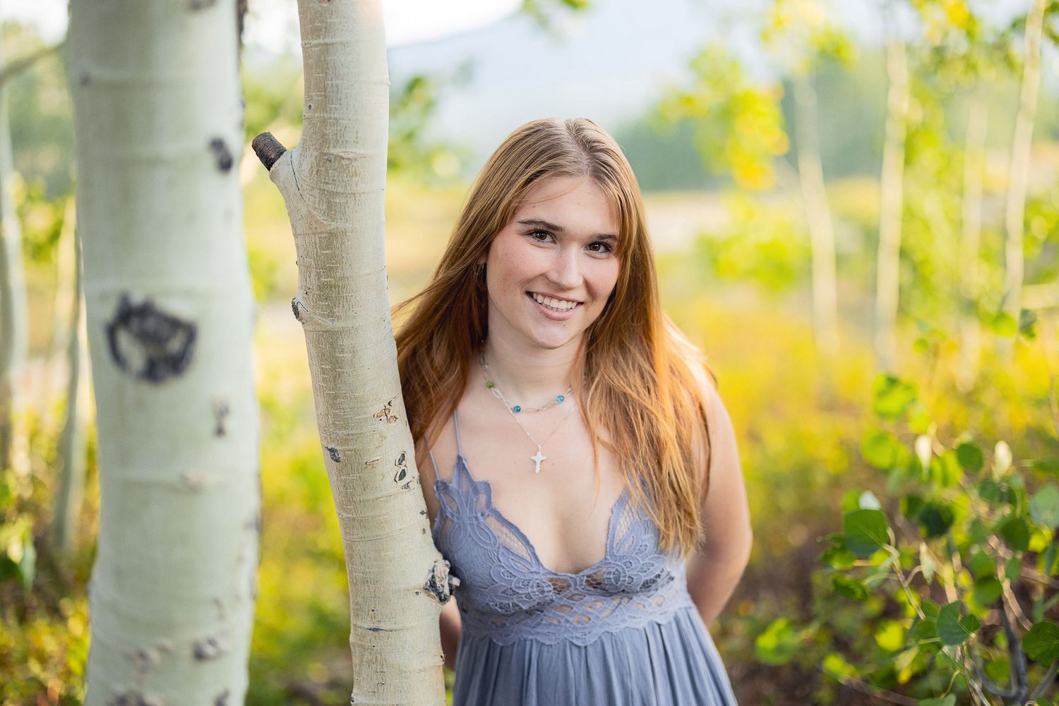 Person in blue dress posing near aspen trees in golden sunlight.