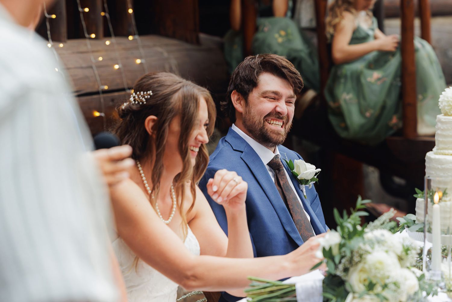 A couple shares a tender moment during their wedding reception as guests celebrate in an outdoor garden setting.