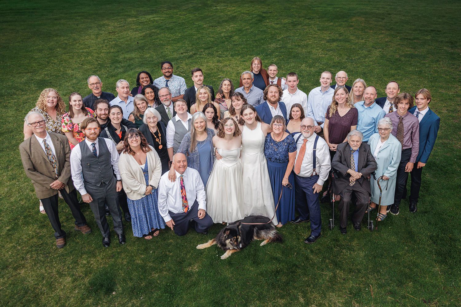 Large group of wedding guests pose together on green lawn for outdoor group photos.