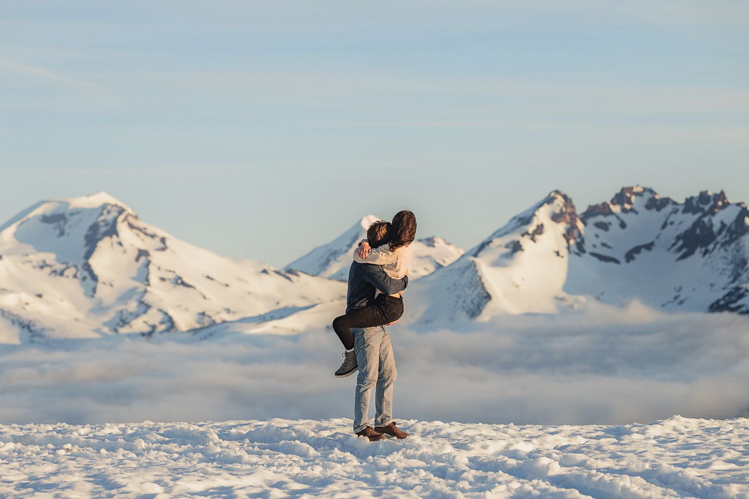 Snow-capped mountain peaks rise above a cloudy valley in a stunning winter alpine landscape.