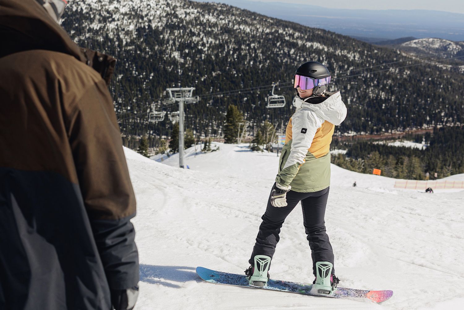 A person in winter clothing is skiing down a snowy mountain slope with a ski lift visible in the background.