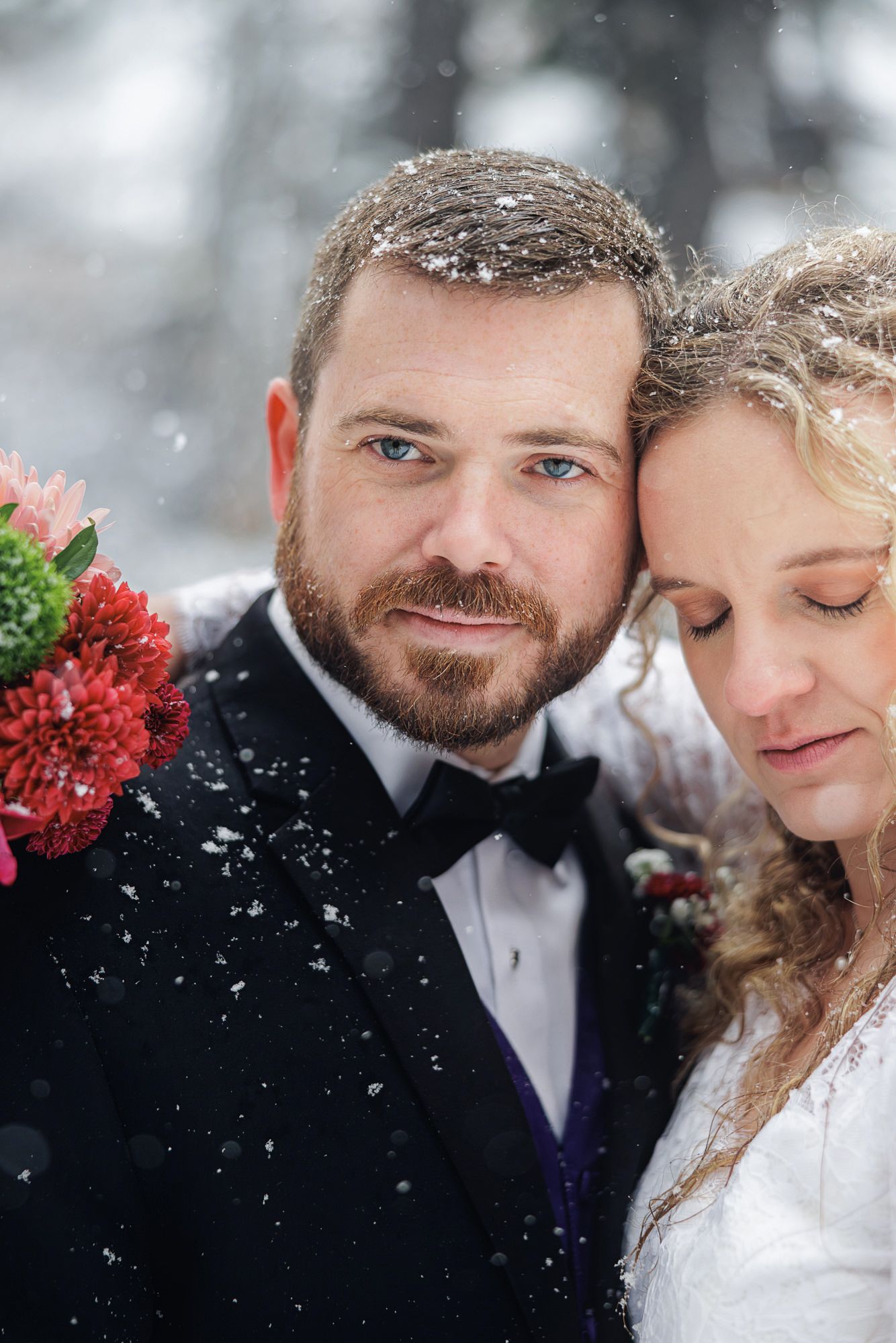 A romantic winter wedding photoshoot with snow falling in a snowy forest setting.