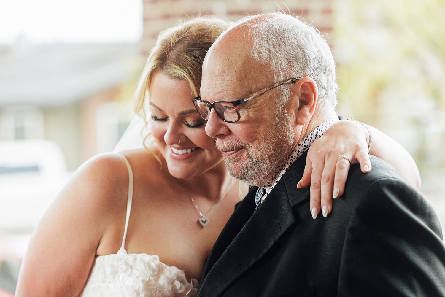Bride in white dress embraces older man in black suit, sharing a tender moment at a wedding celebration.
