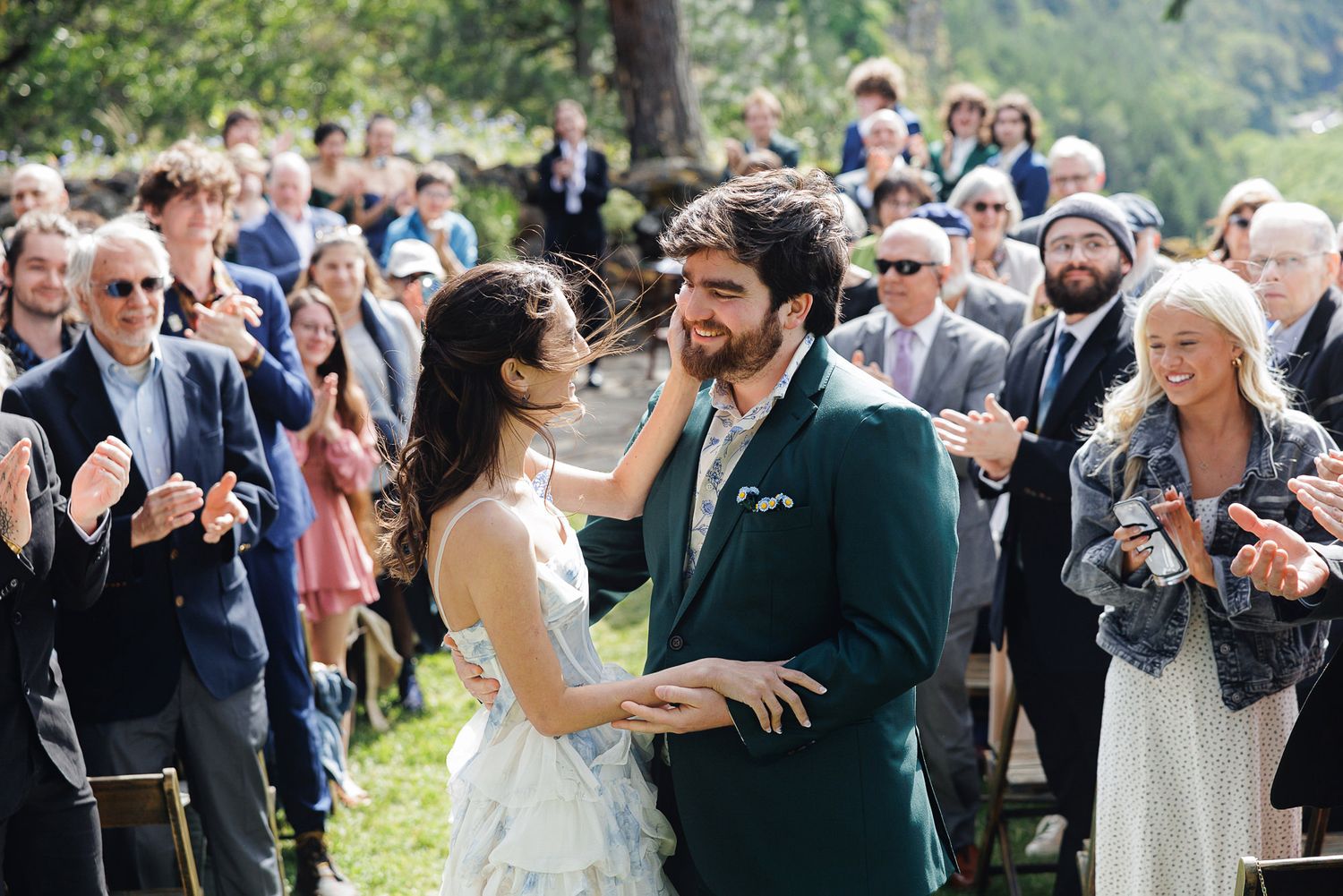 Joyful newlyweds share a tender moment walking back down the aisle as wedding guests clap and celebrate outdoors.