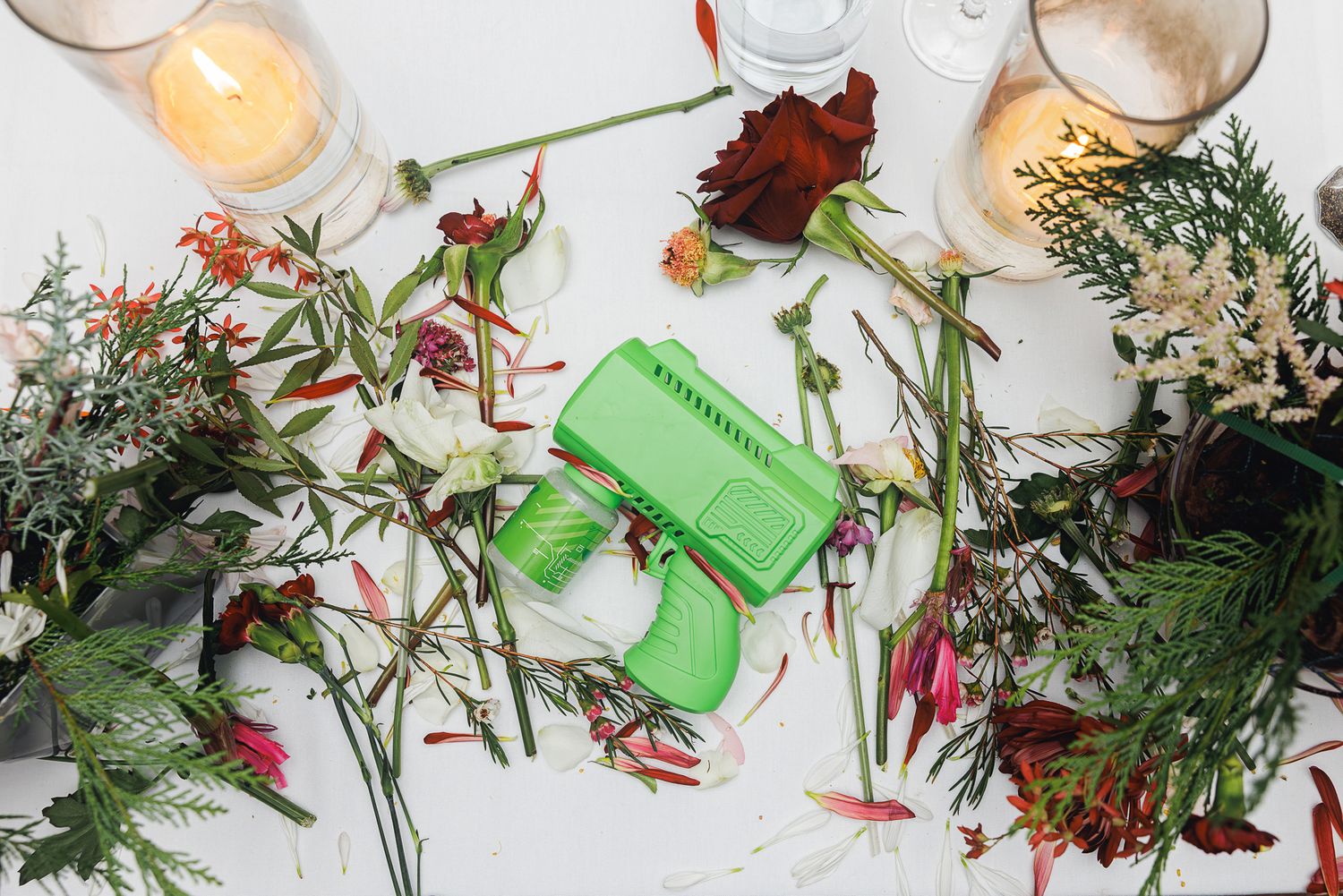Dried red rose petals and green leaves scattered on a white surface with green plastic objects.