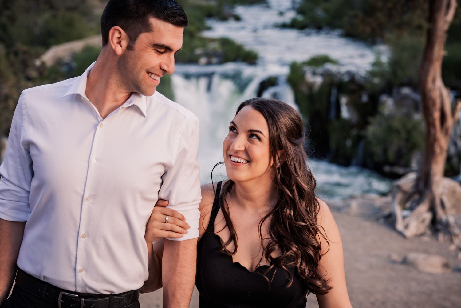A couple shares a romantic moment while sitting outdoors in a natural setting during golden hour.