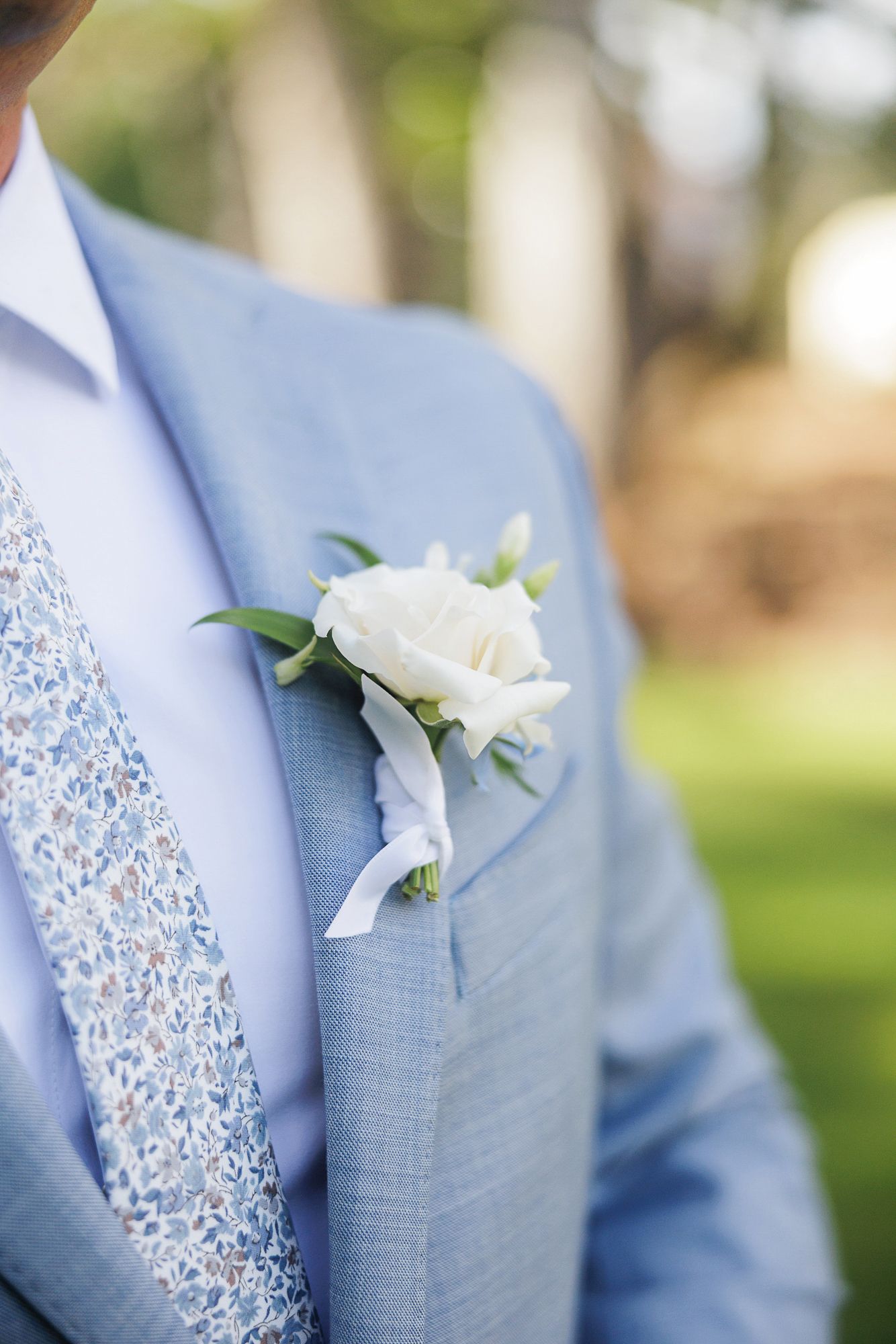 White rose boutonnieres pinned to light blue suit jackets in a wedding party lineup.