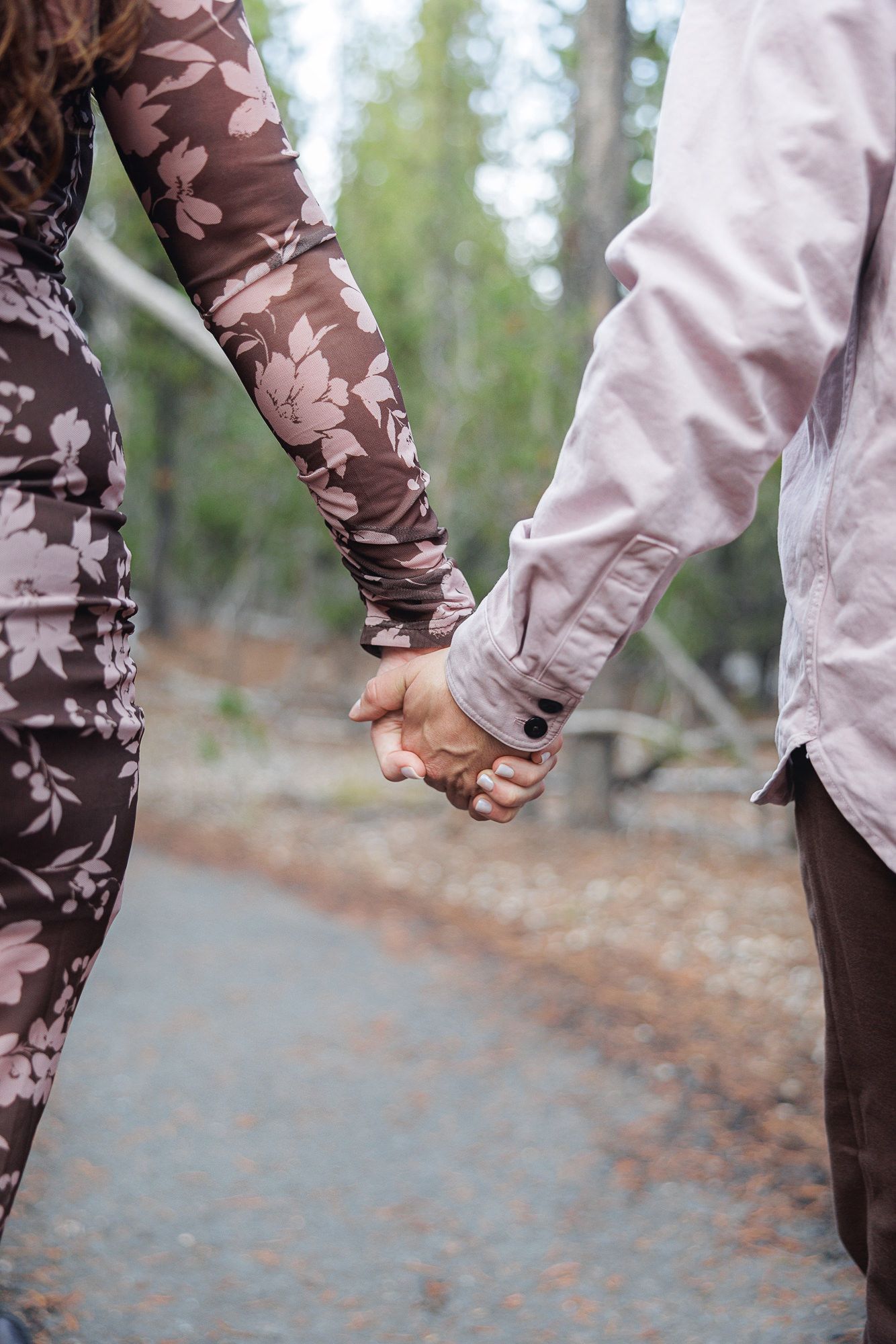 Close-up view of two people holding hands while walking on a path through autumn trees.