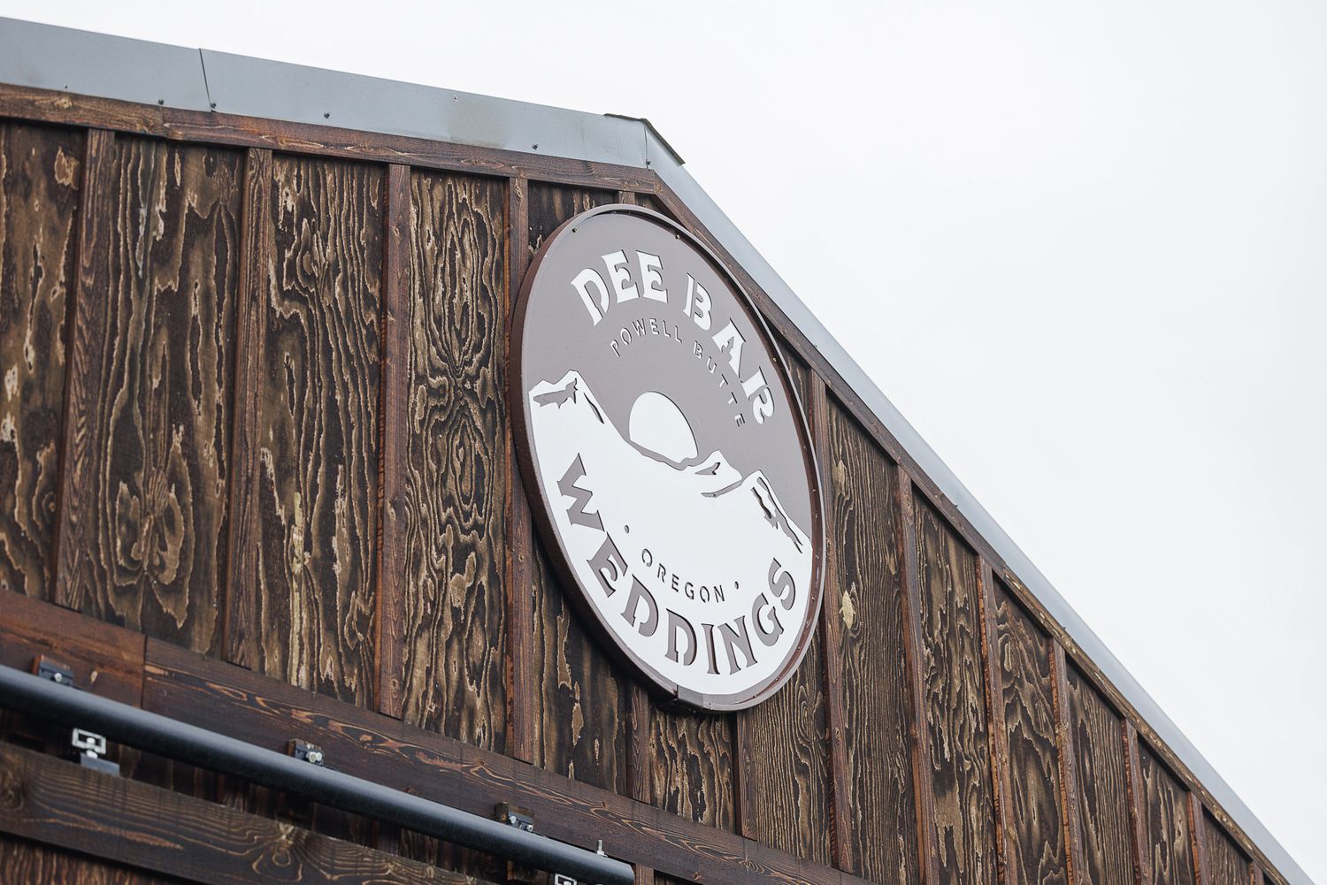 Dee Bar Weddings rustic wooden barn sign in Oregon, featuring mountain and lake logo design.