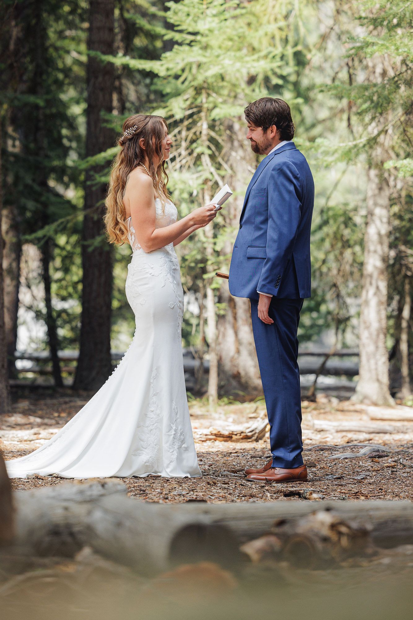 A couple exchanges vows during an intimate forest wedding ceremony surrounded by tall evergreen trees.