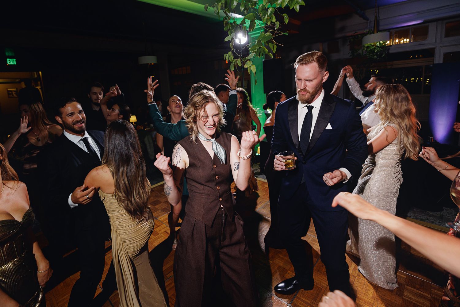 Guests dancing joyfully at a wedding reception, with a couple in the center dressed in formal attire.