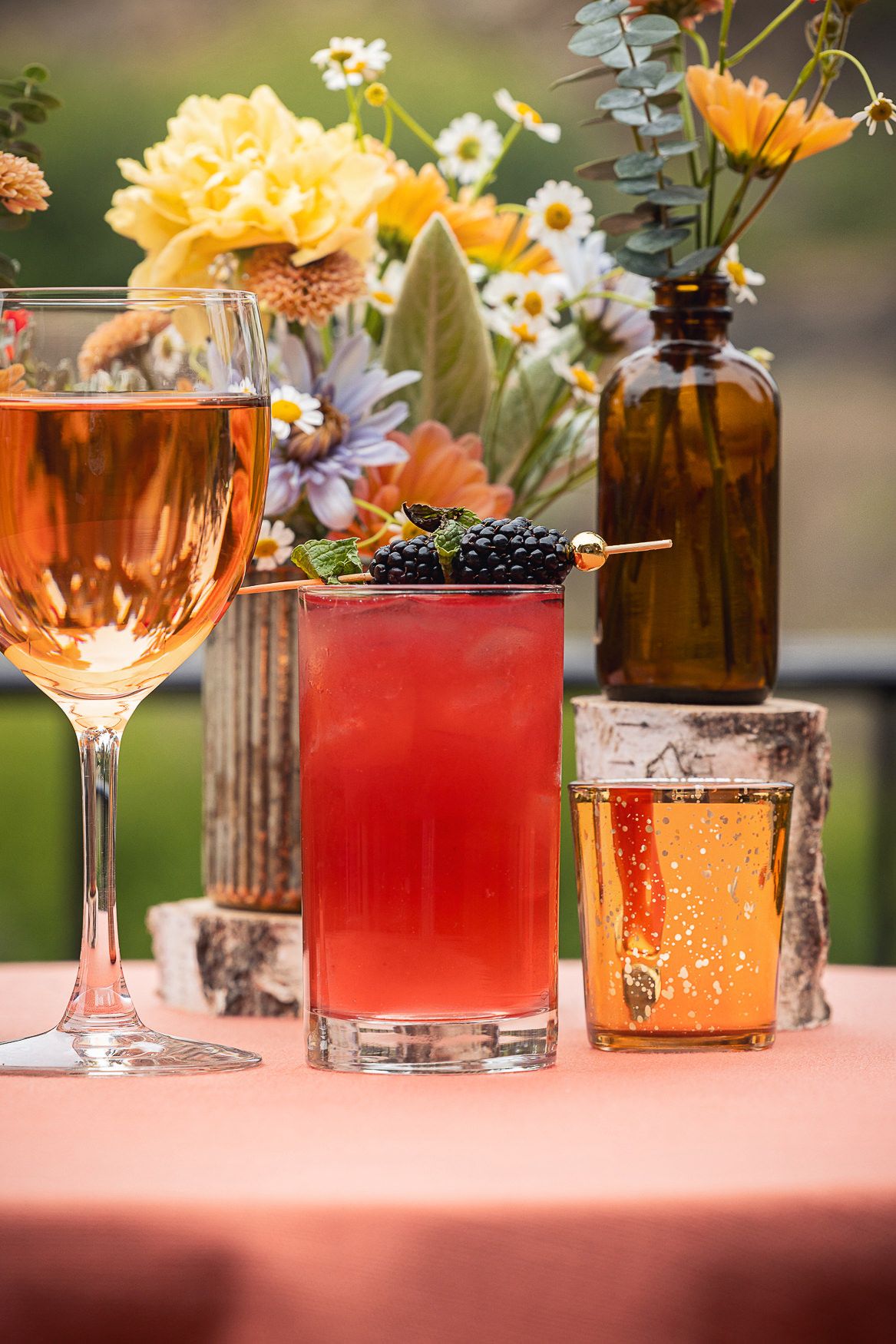 Elegant cocktails and wine glasses arranged with floral decorations on pink tablecloth.