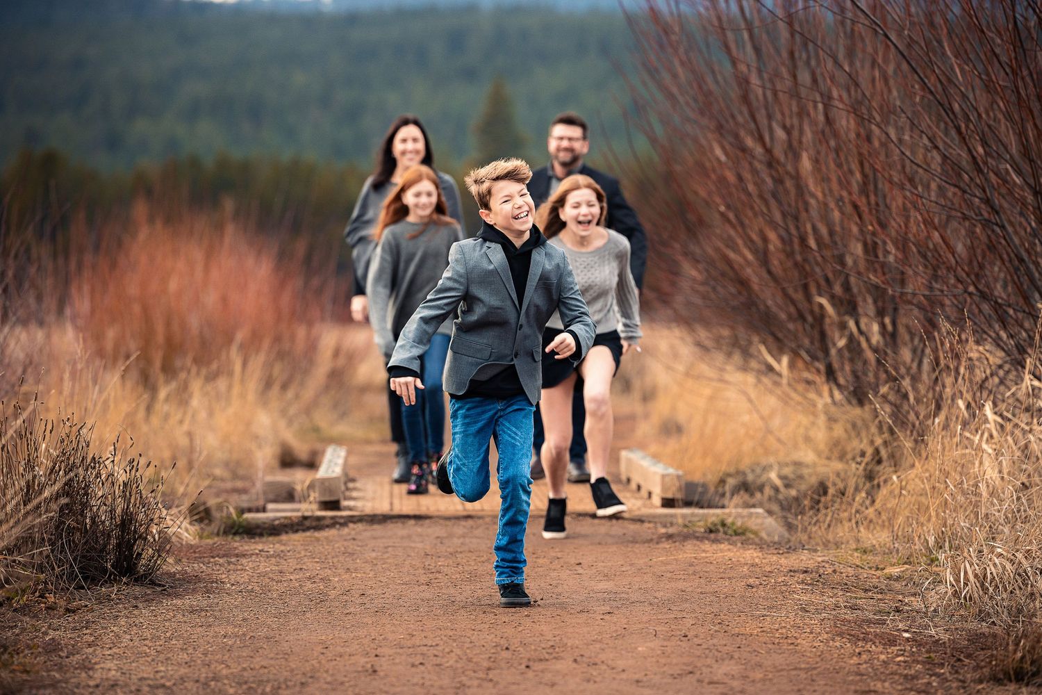 A group running together on a dirt trail through autumn brush with mountains in the background.