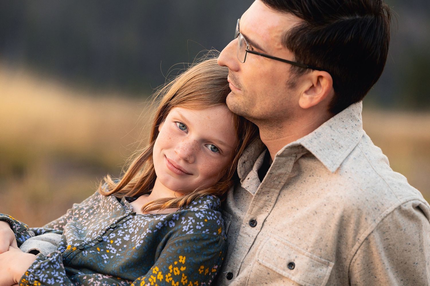 An intimate portrait of a couple sitting in a field during golden hour.
