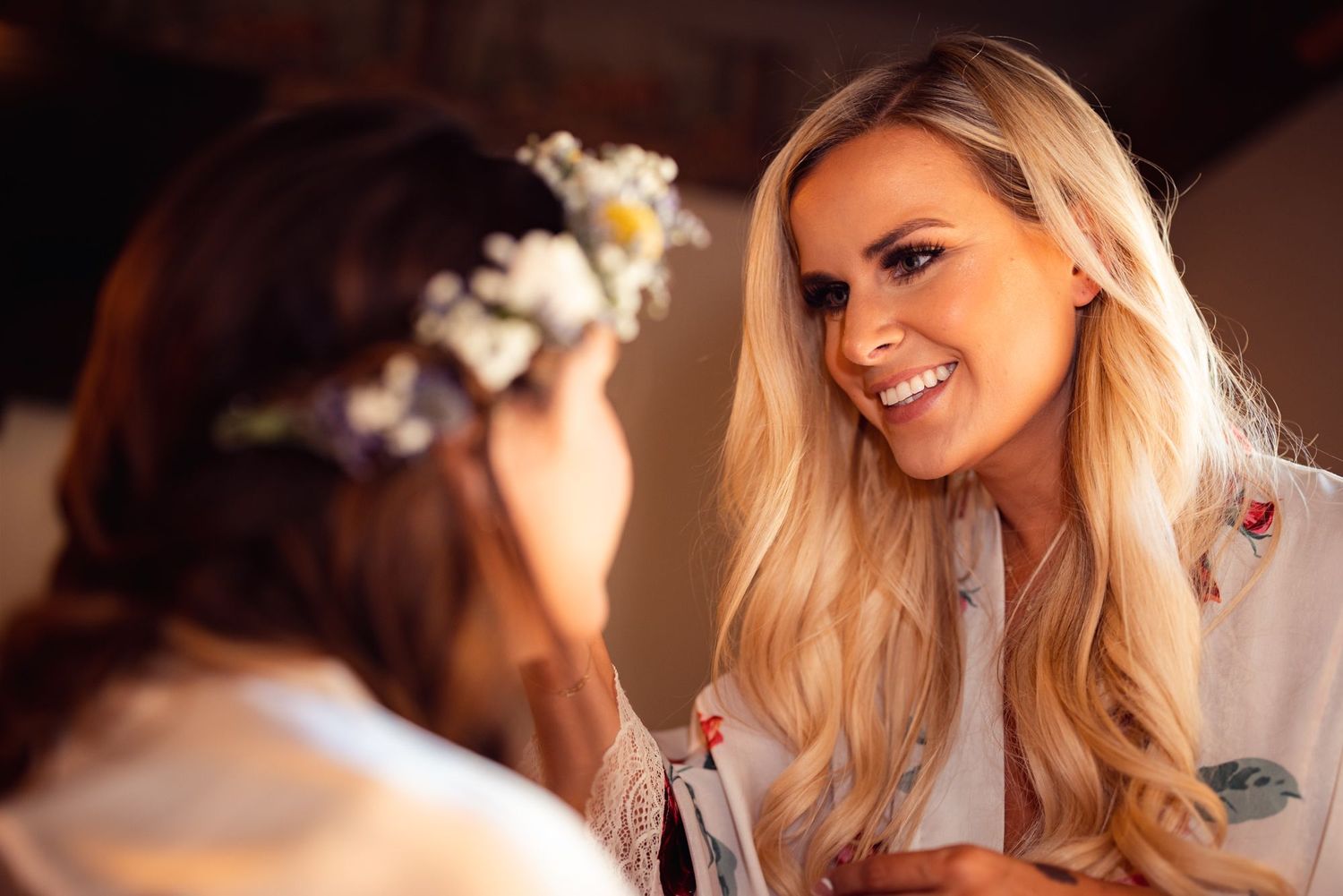 Two people wearing floral crowns share a joyful moment in warm lighting.