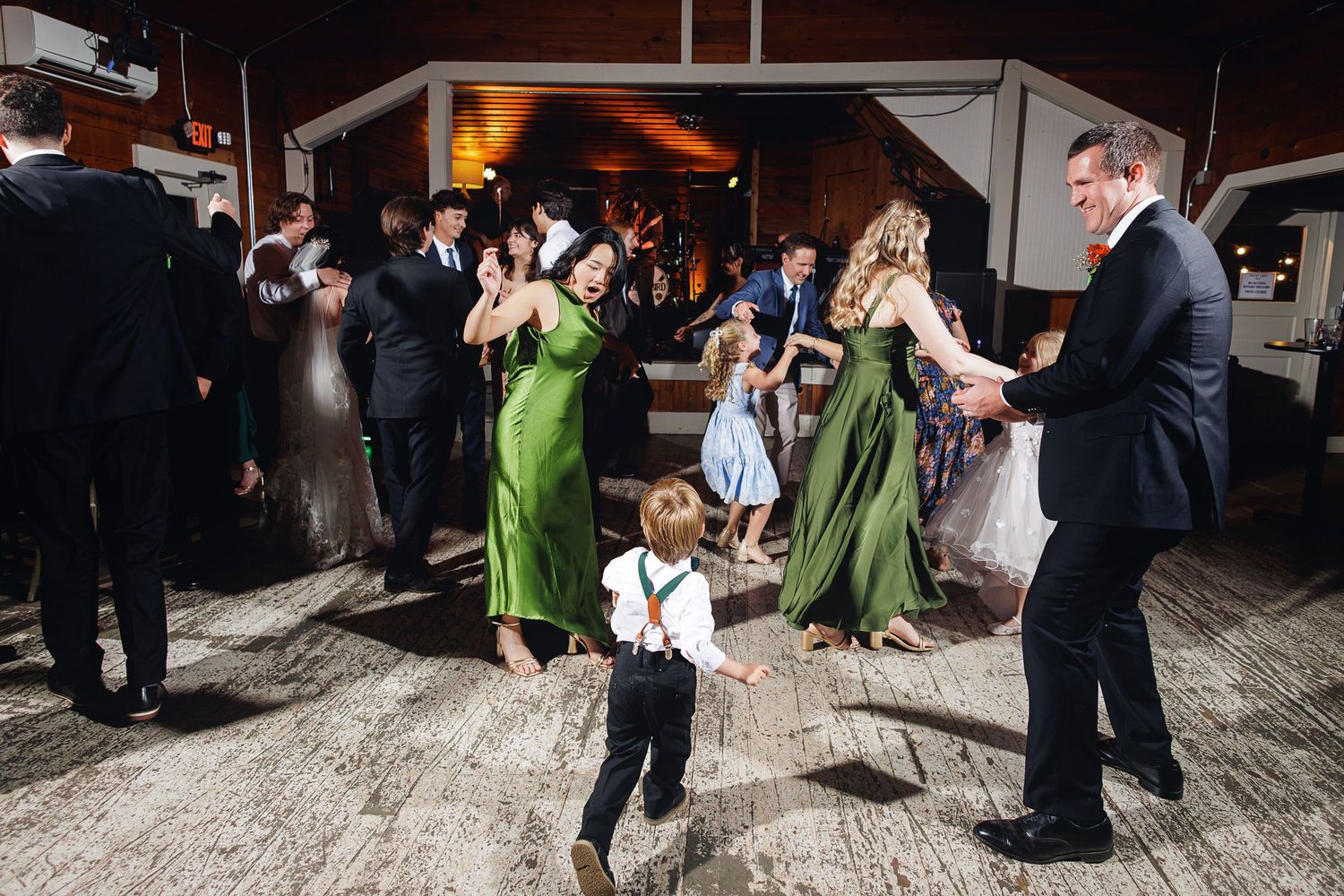Wedding reception guests dancing joyfully, featuring a young boy in suspenders on the dance floor.