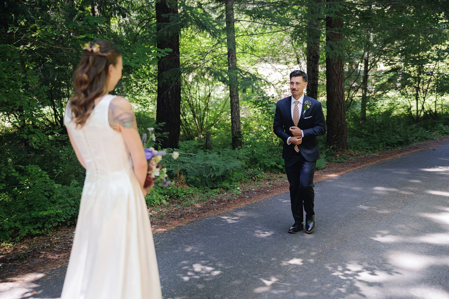 A couple sharing their first look on a wooded path, with one in a white dress and the other in a navy suit.
