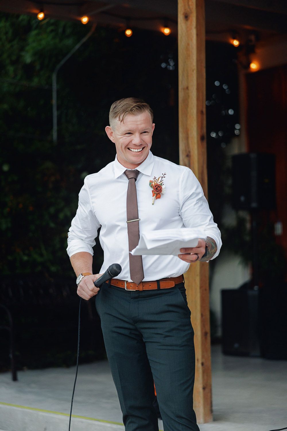 A person in a white dress shirt and dark pants laughs joyfully during what appears to be an outdoor event.