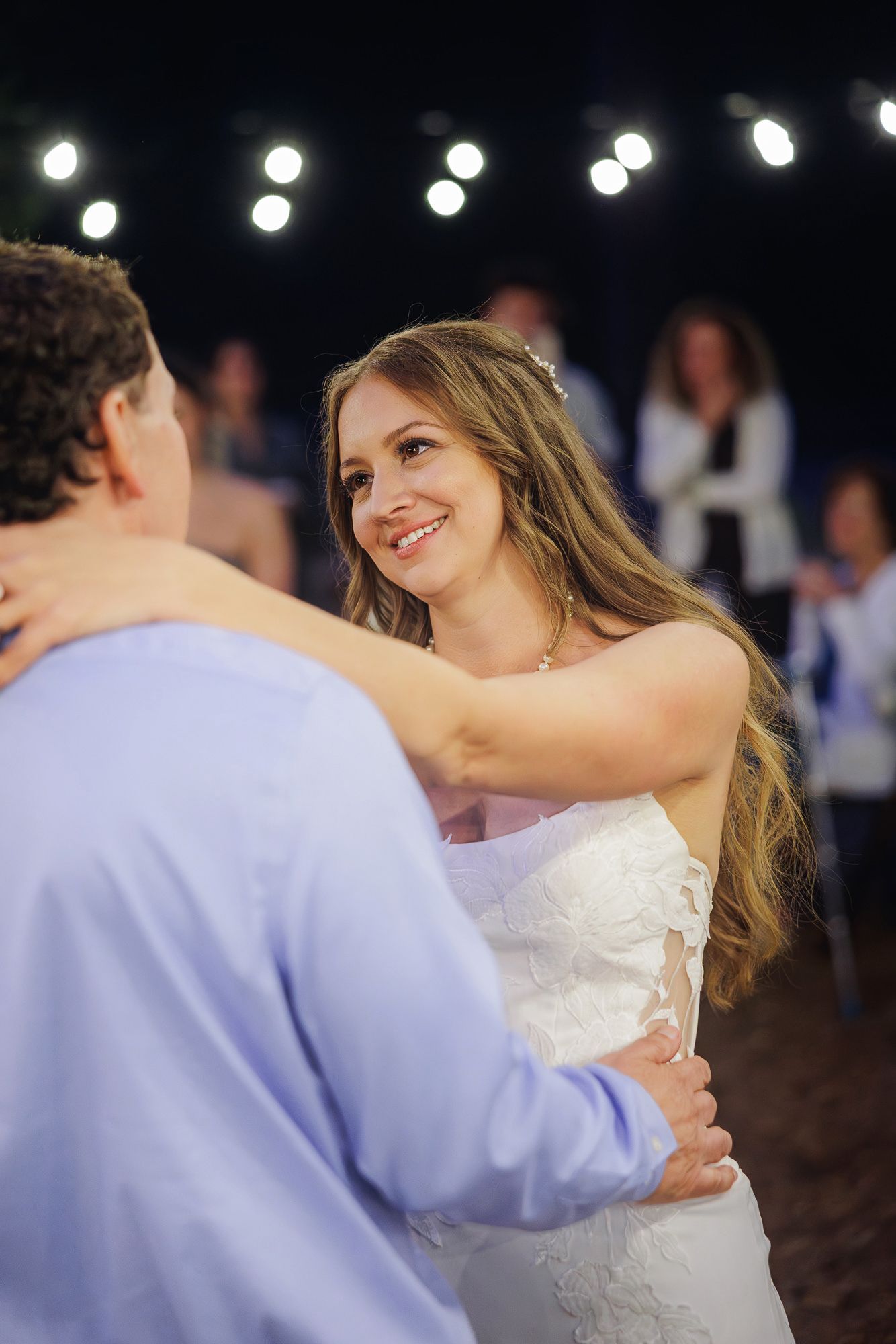 A couple shares a romantic dance at their wedding reception with twinkling lights in the background.