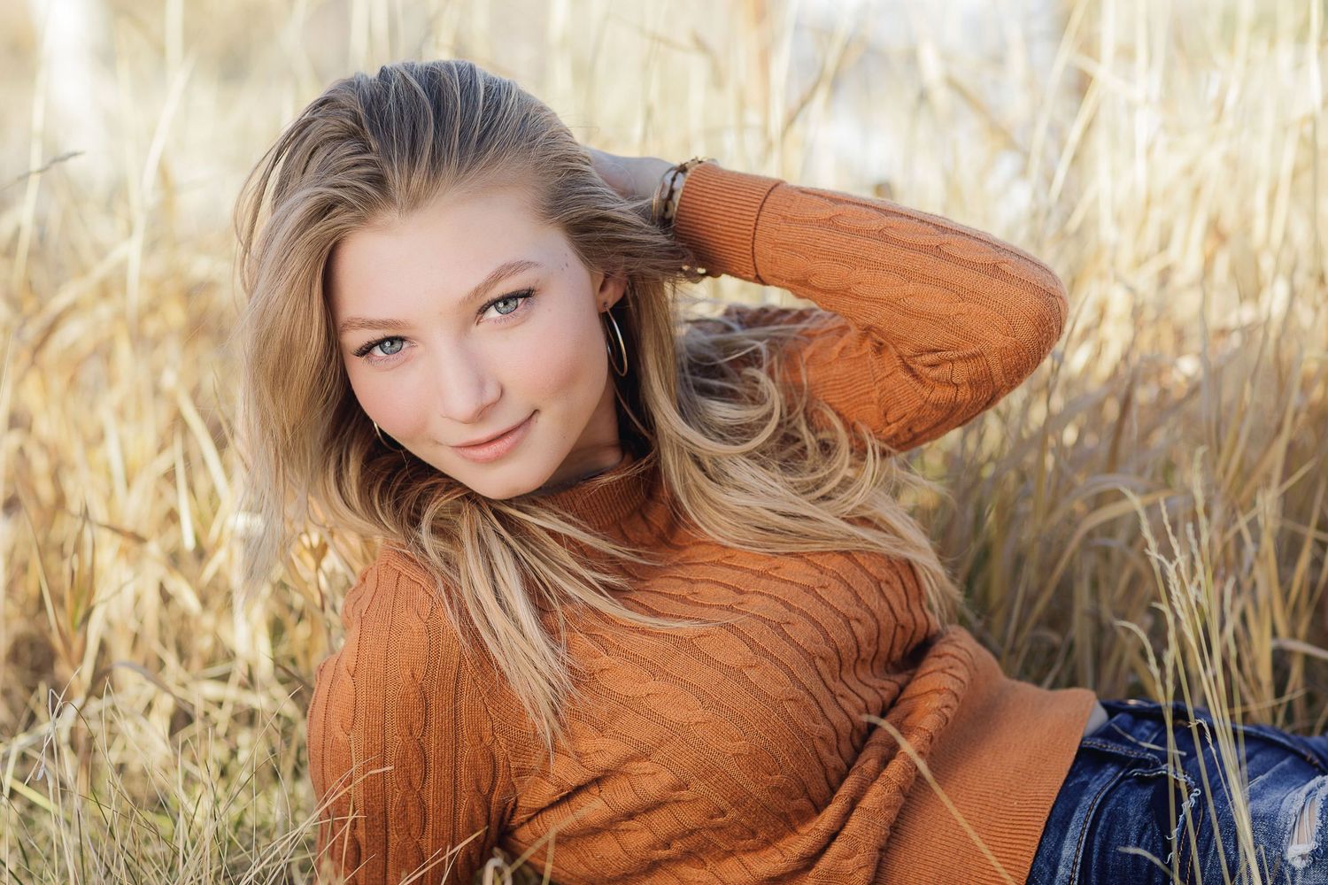 Person in orange sweater laying in golden autumn grass field.