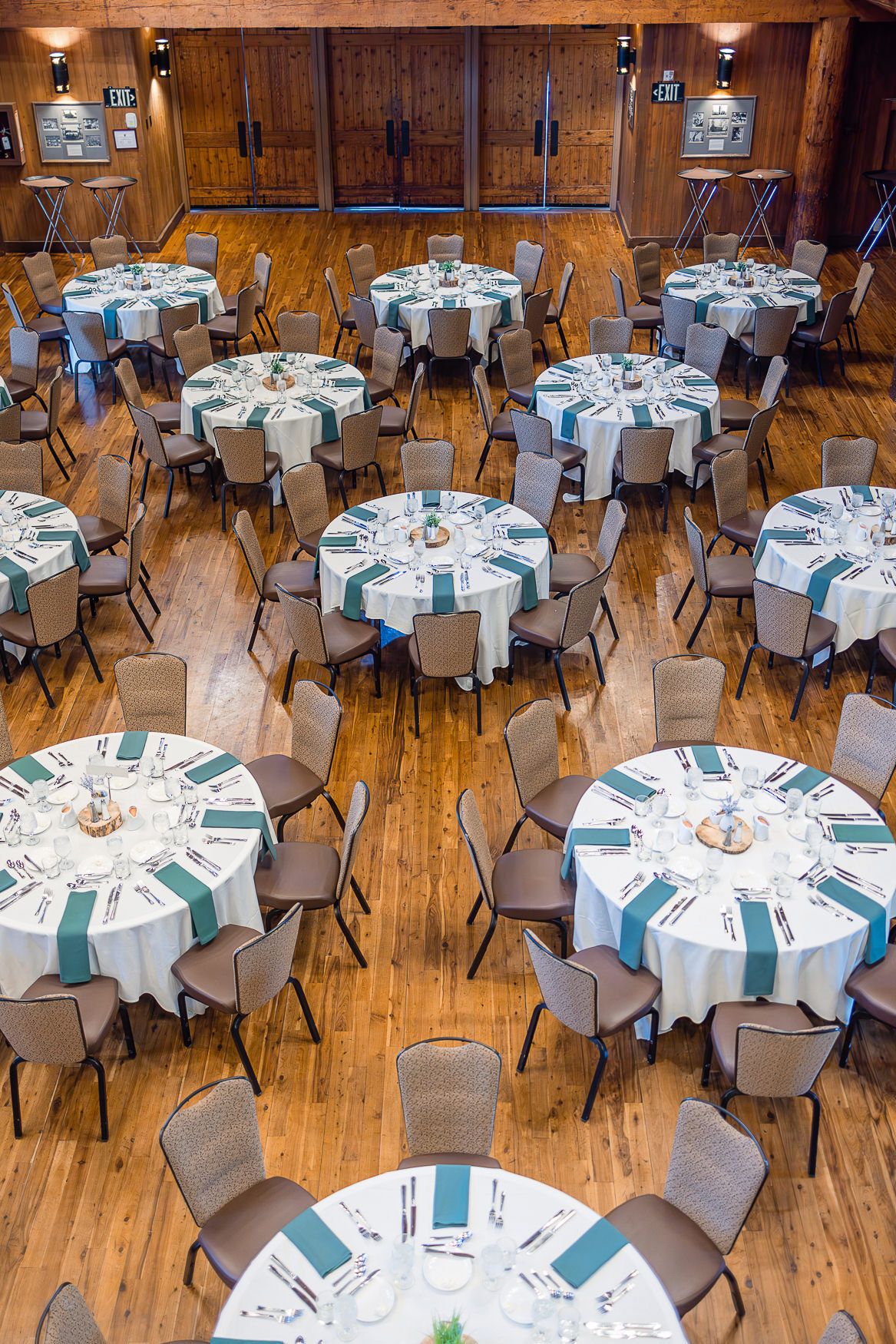 Overhead view of an elegant reception setup with round tables and teal accents on wooden flooring.
