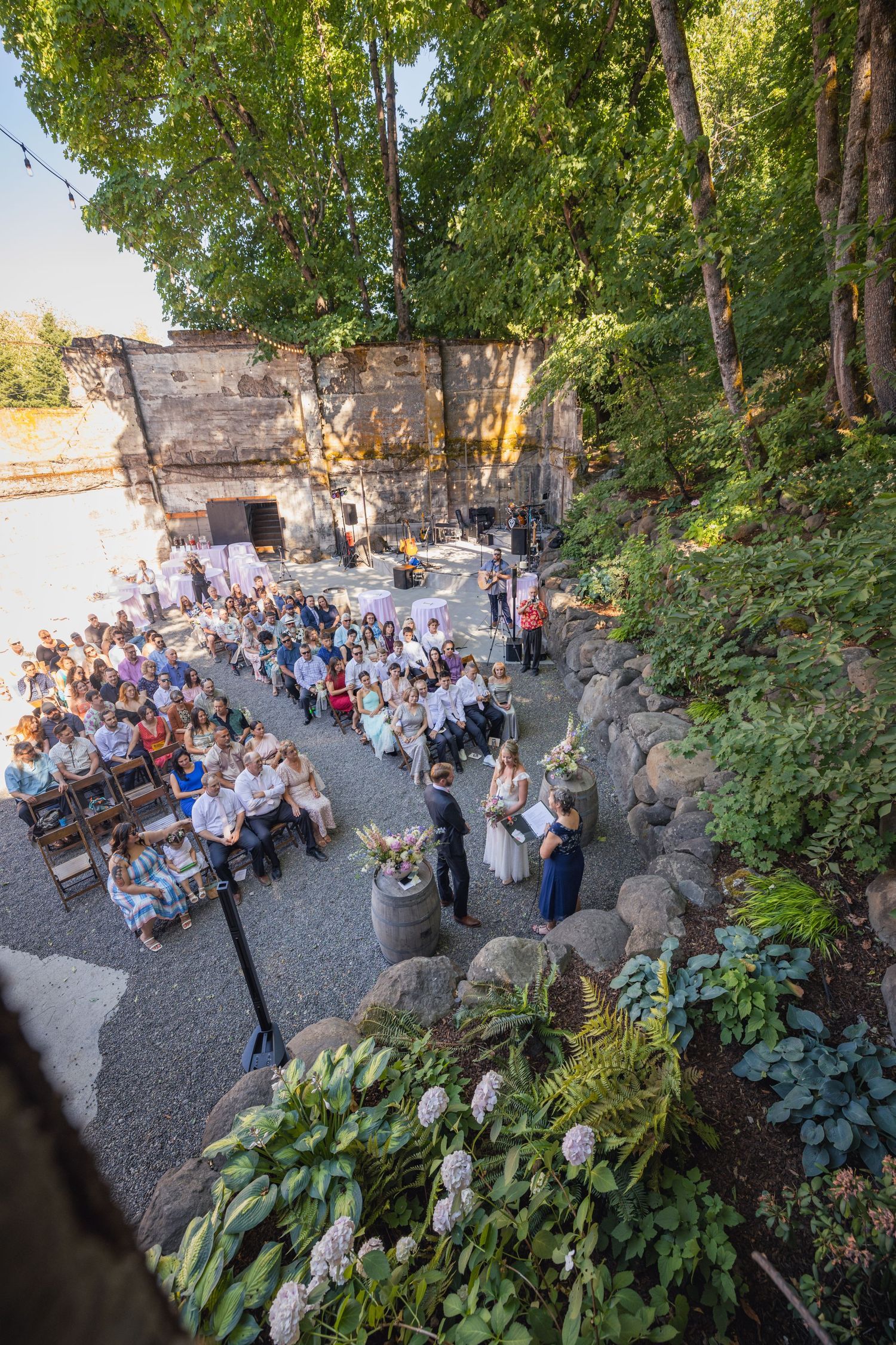 Large outdoor event venue with stone walls and trees showing a crowded dining area during golden hour.
