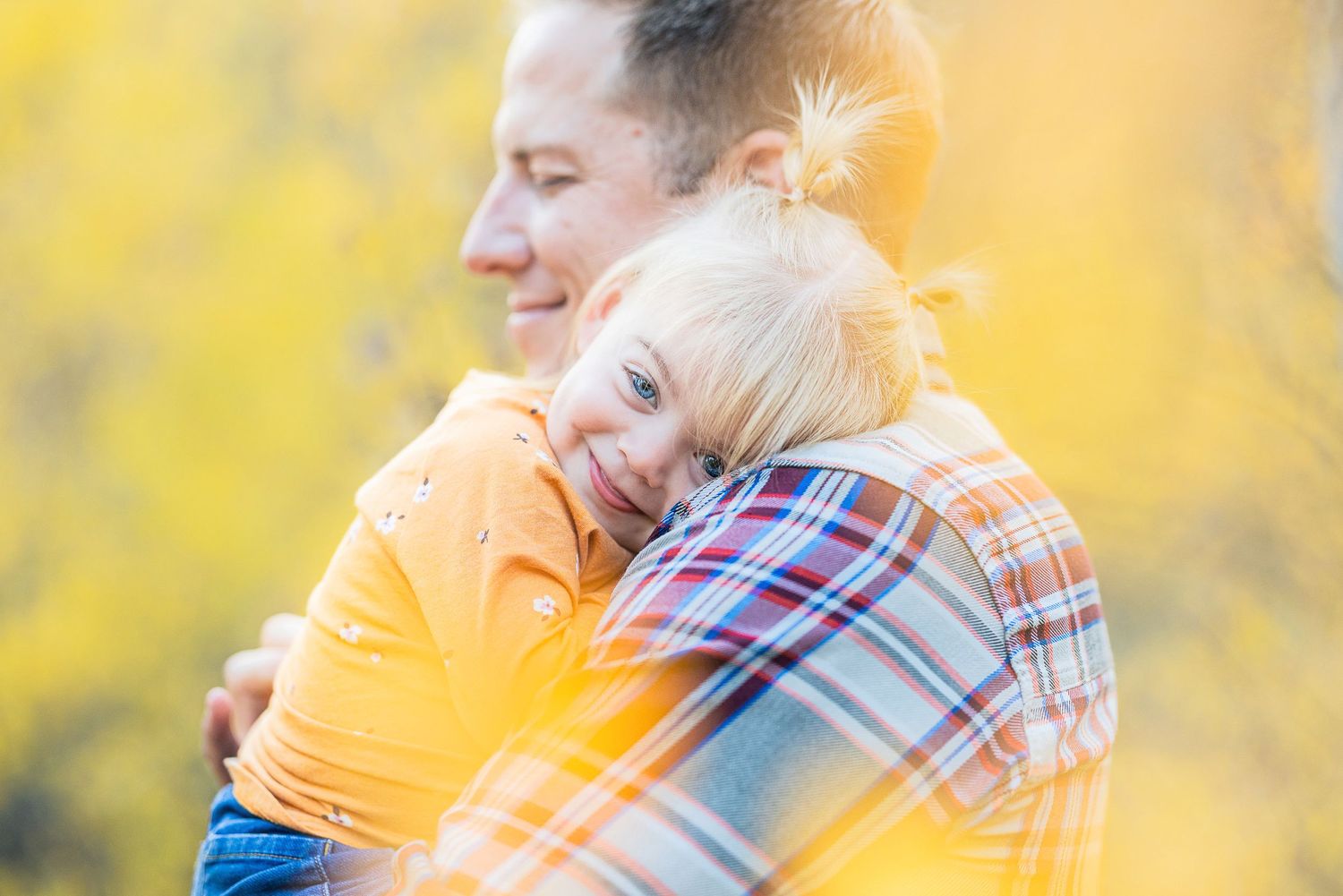 Tender embrace between parent and child against soft yellow background.