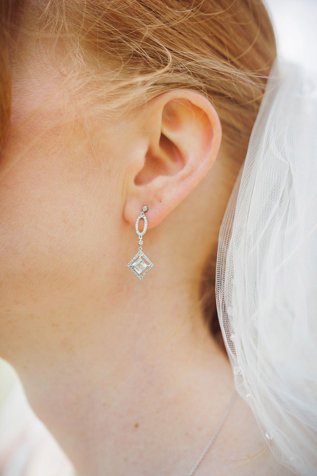 Close-up of a bride wearing an elegant diamond drop earring with a square pendant and white veil.