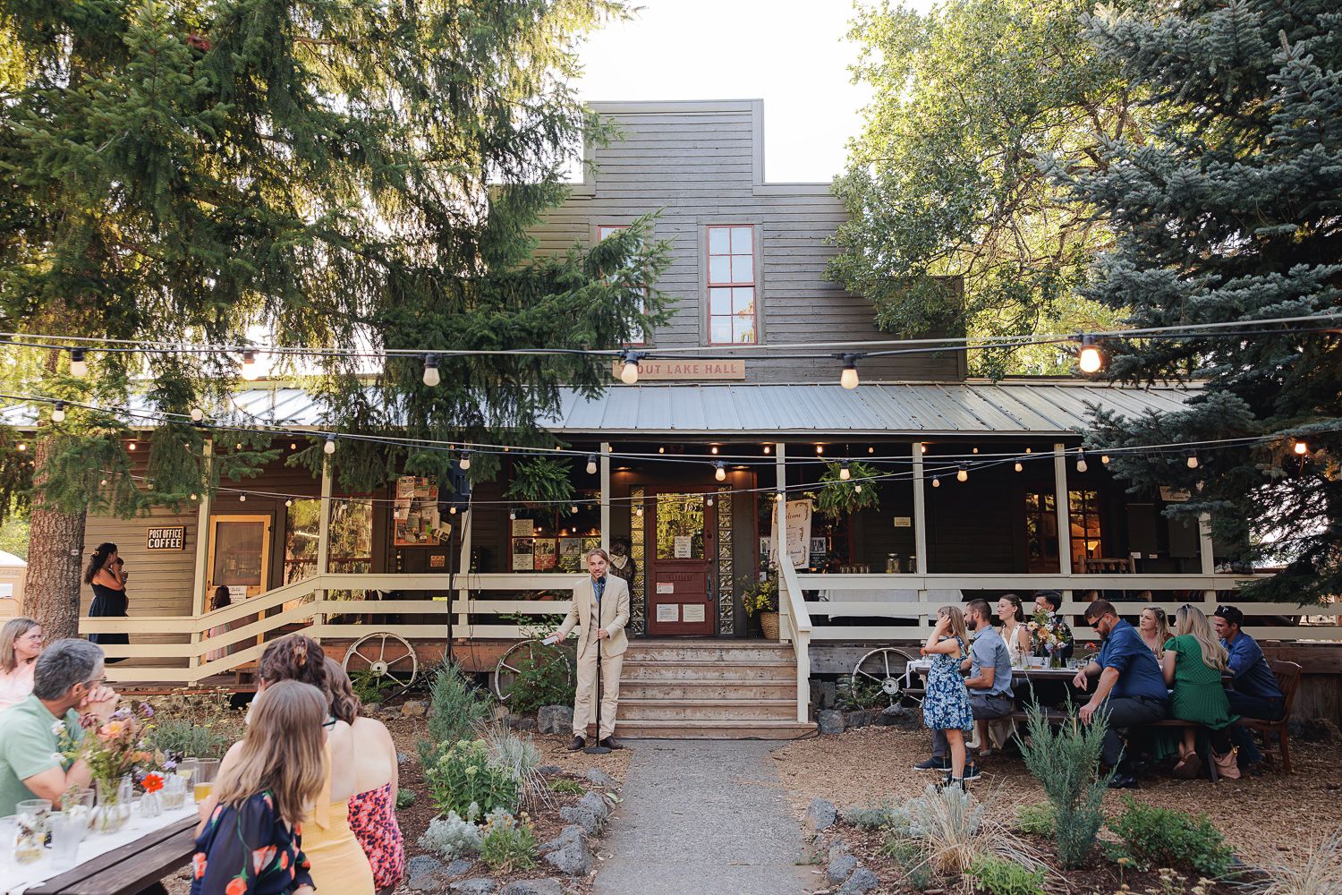 An outdoor patio dining area surrounded by trees and string lights creates a cozy restaurant atmosphere at dusk.