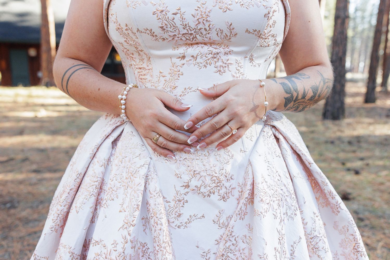 Close-up details of a white wedding dress with delicate pink floral embroidery pattern.