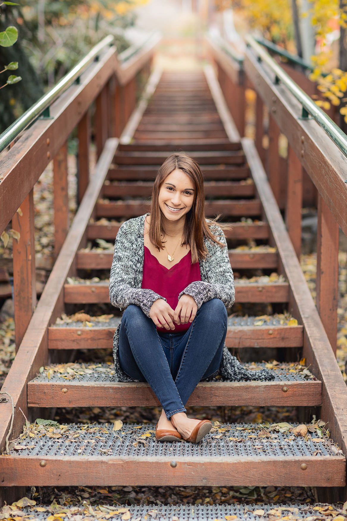 A casual portrait on wooden stairs surrounded by fall foliage.