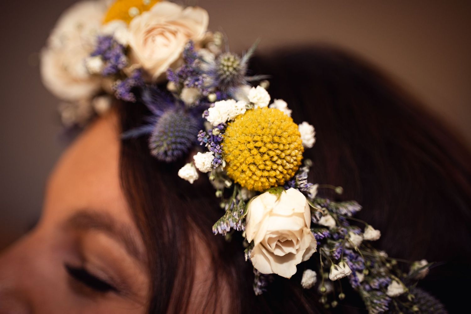 Closeup of a floral crown with yellow, white and purple blooms against a dark background.