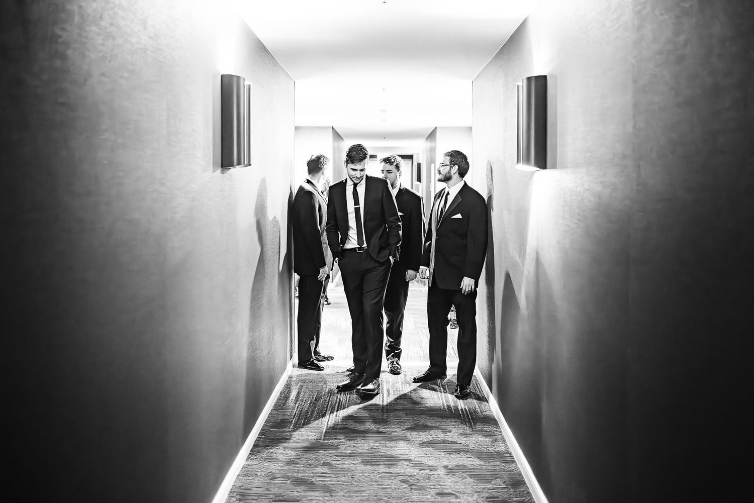 A black and white photograph showing a group of suited men standing and conversing in a narrow hallway.