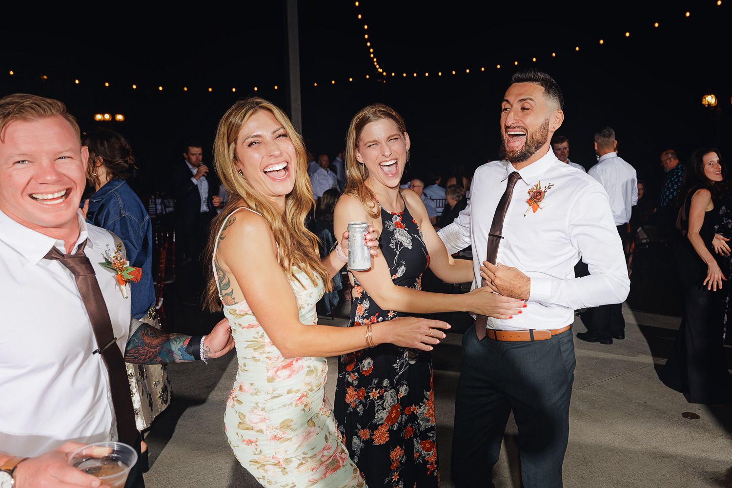 People dancing and celebrating at a nighttime outdoor party with string lights overhead.