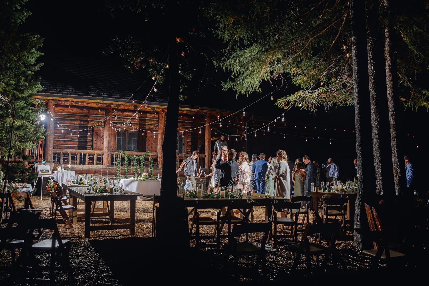 An outdoor wedding venue setup with wooden chairs arranged in rows beneath tall trees at dusk.
