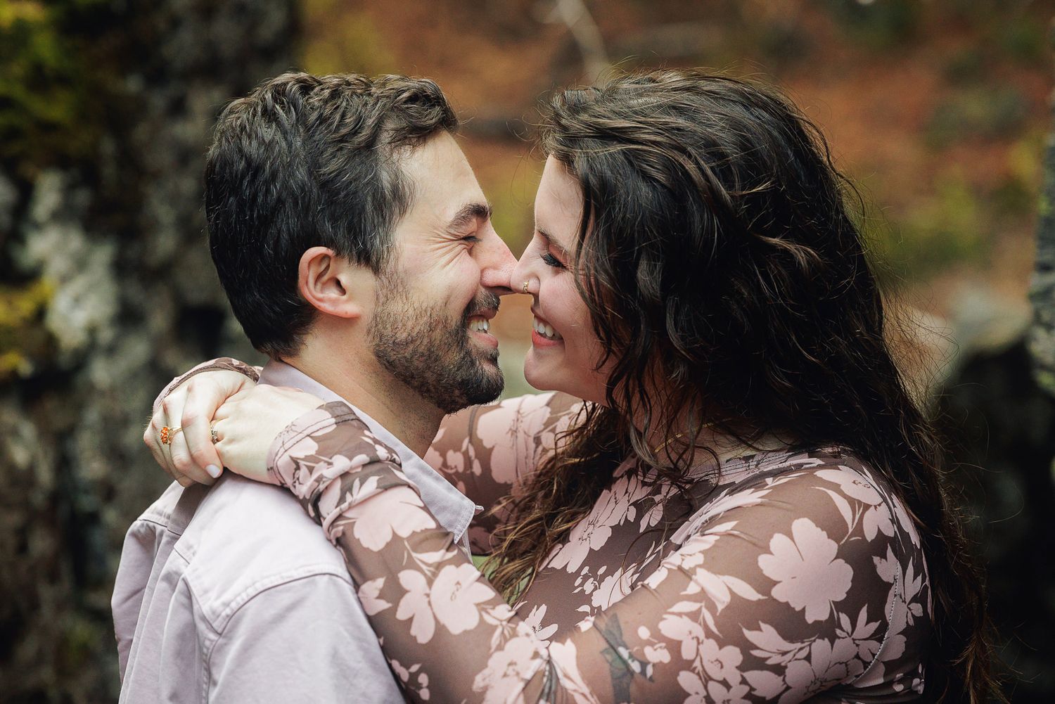 Romantic couple sharing intimate moments in an autumn forest setting with blurred bokeh background.
