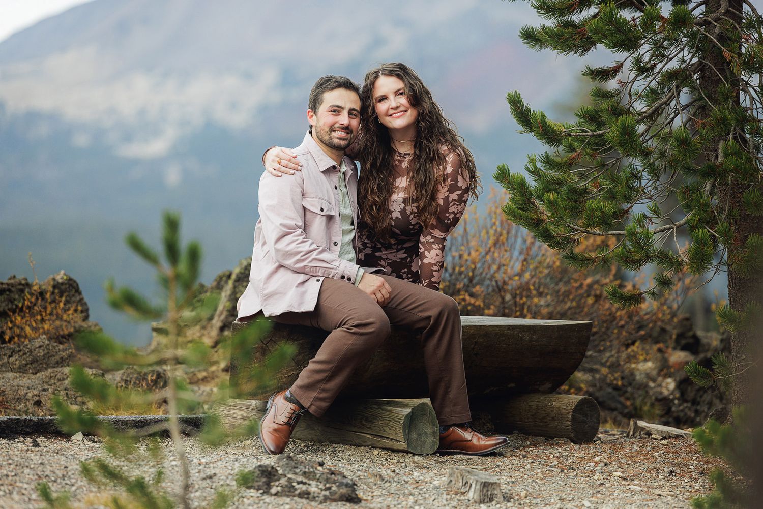 A couple sits together on a rocky mountain overlook enjoying scenic mountain views in the distance.