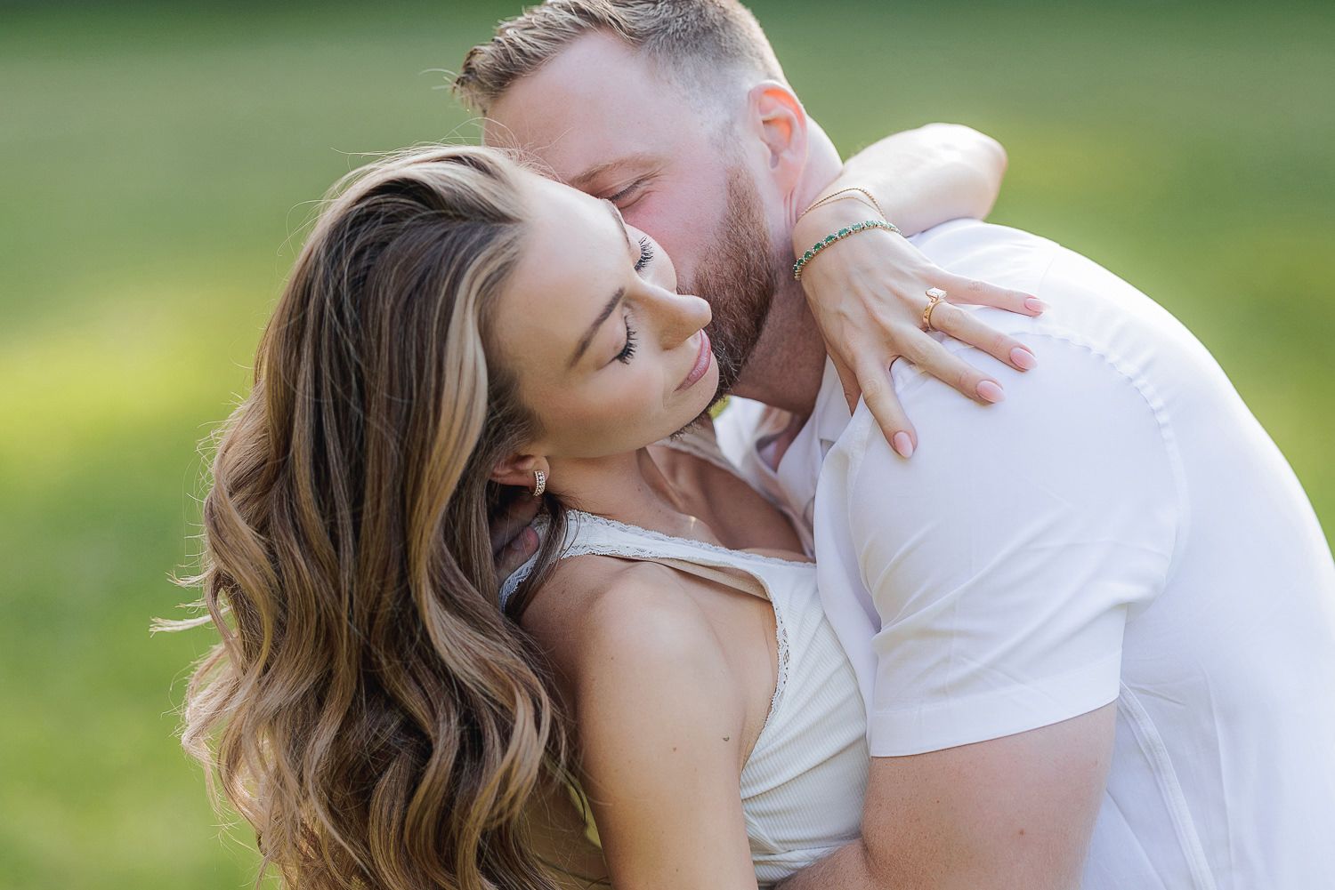 Romantic couple shares tender kisses in outdoor setting with soft natural lighting on sunny afternoon.