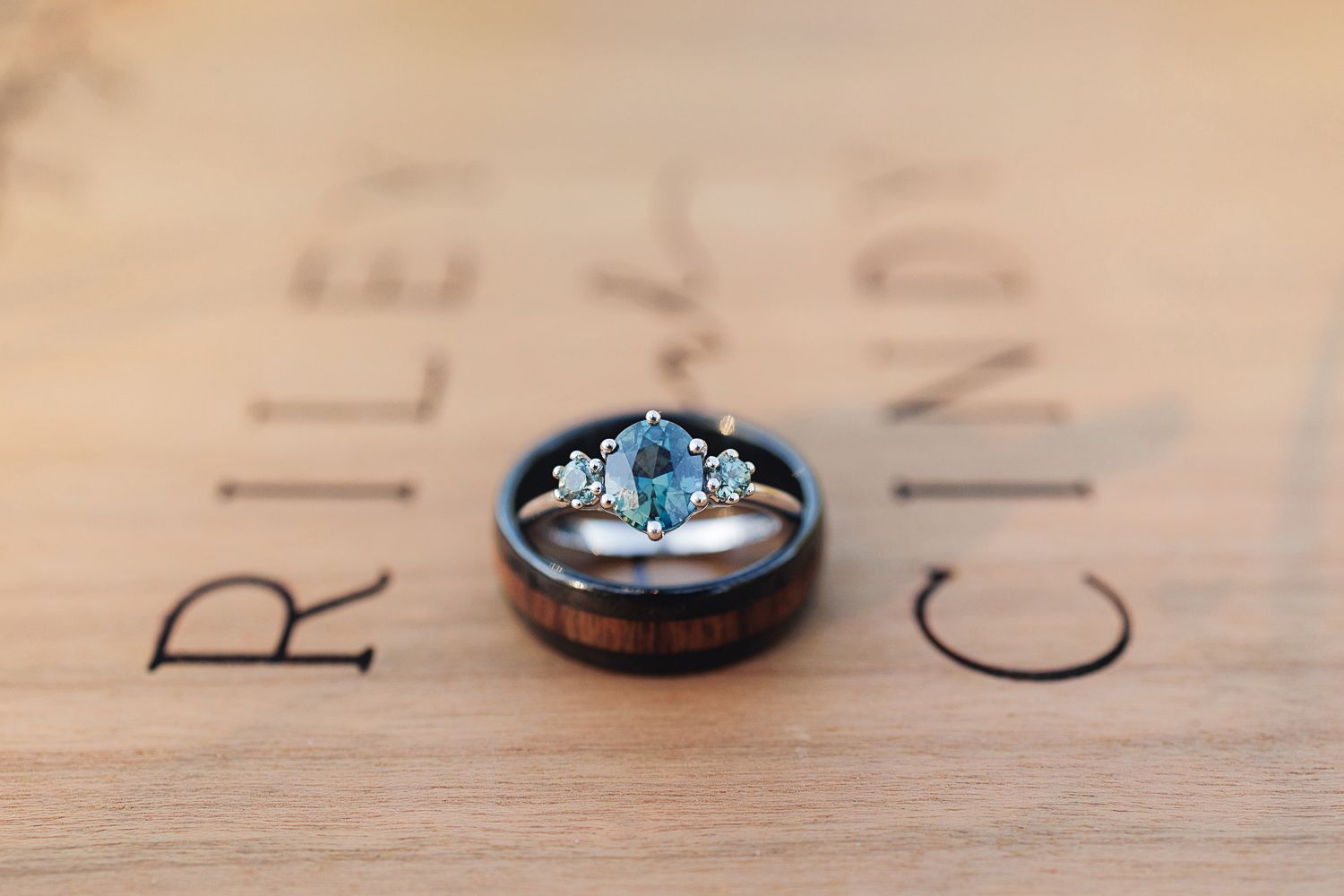 Wedding rings with a blue topaz or aquamarine engagement ring displayed on wooden surface with text in background.