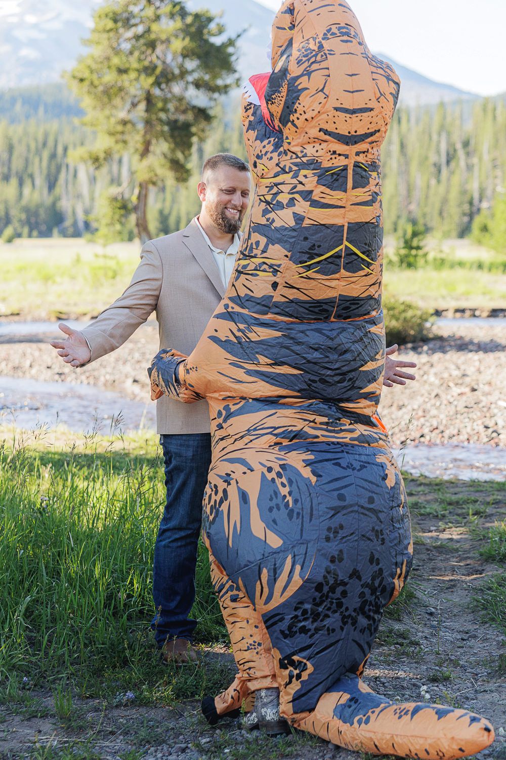 A playful engagement shoot featuring an inflatable T-Rex costume in a mountain landscape setting.