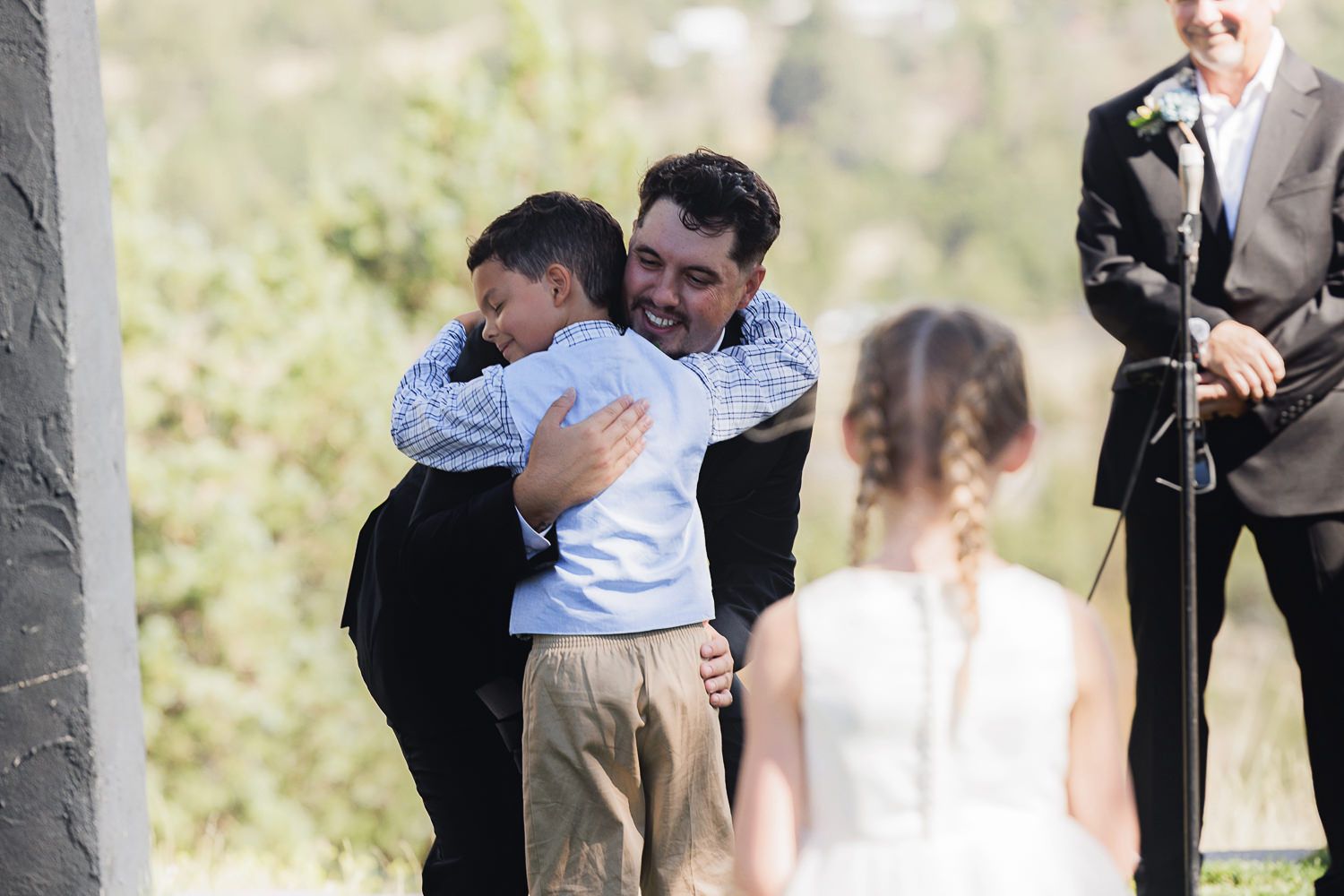 Two people share an emotional embrace at an outdoor gathering while others look on in the background.