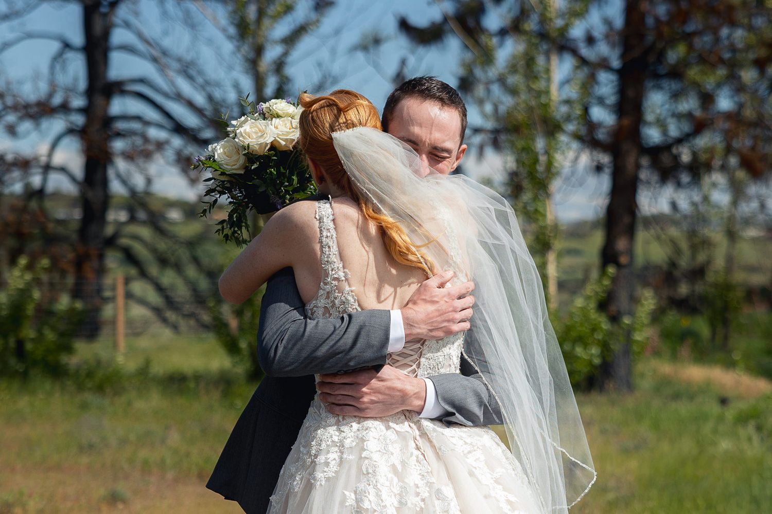 Bride and groom share a tender embrace outdoors on their wedding day, bride holding white bouquet.