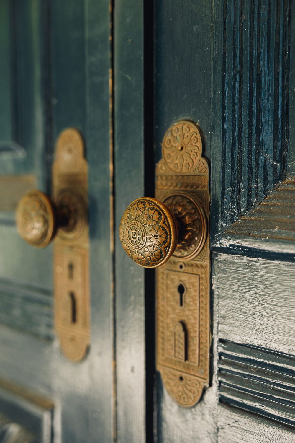 A series of antique brass door knobs and locks on dark blue vintage wooden doors shown in detail.
