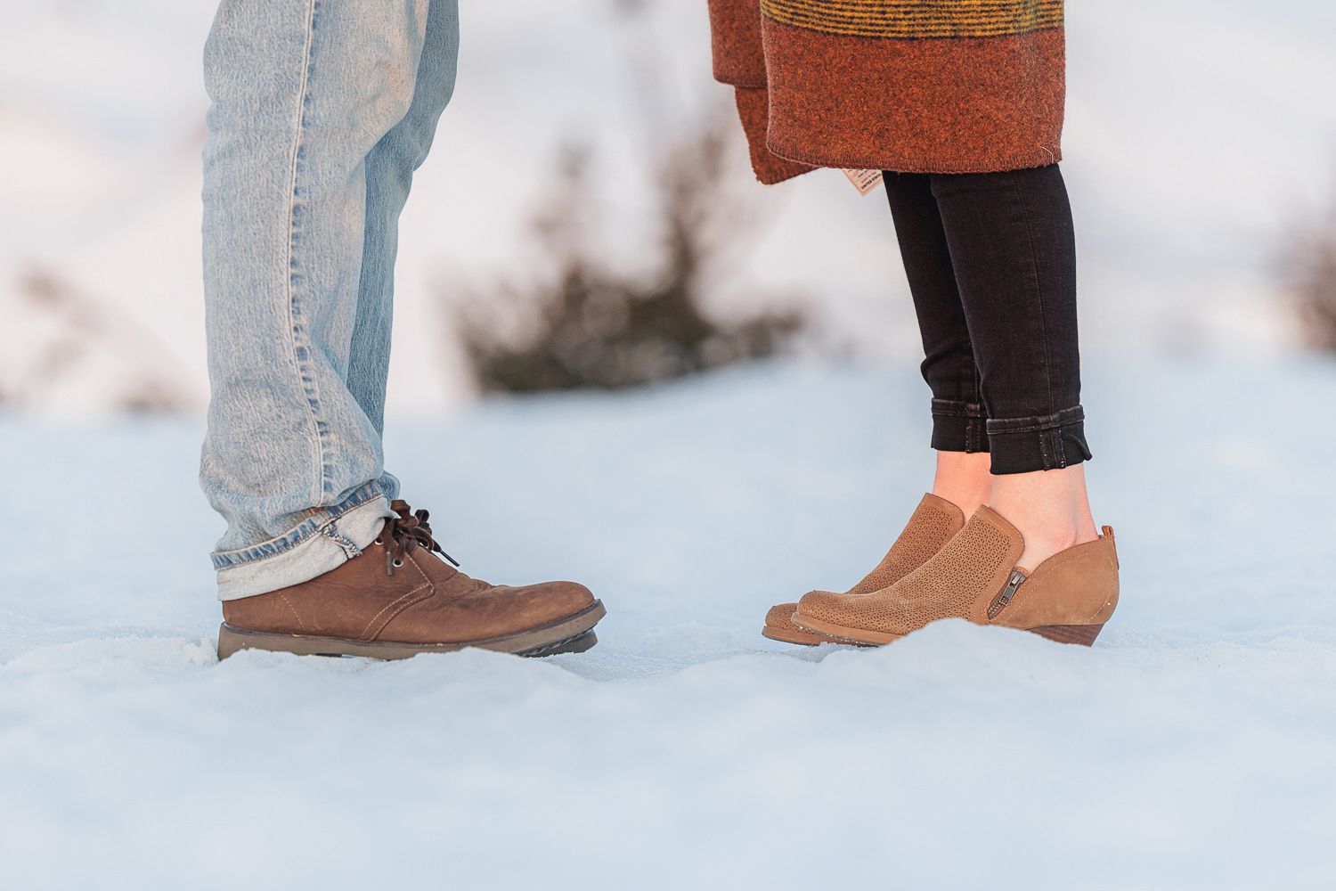 Close-up view of legs and feet of people standing in snow wearing winter boots and jeans.