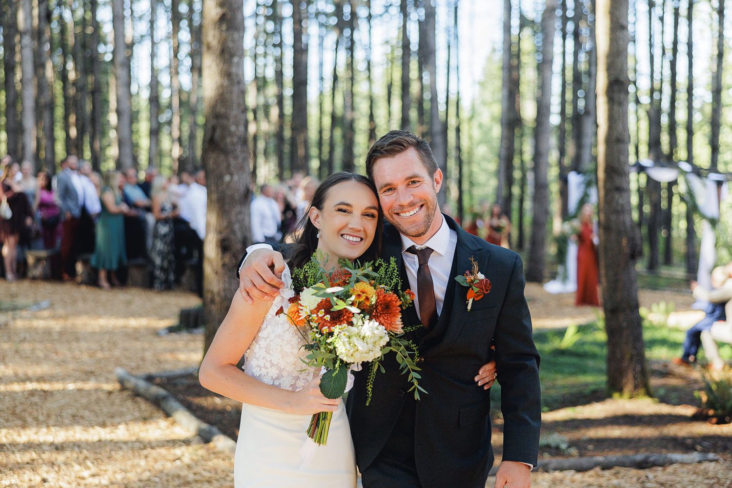A couple shares intimate moments during their outdoor wedding ceremony in a sunlit pine forest.