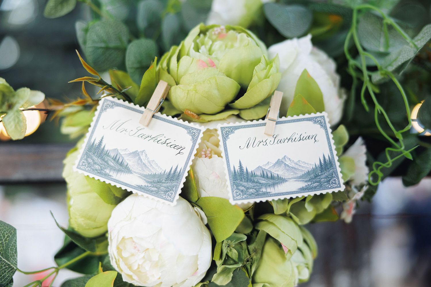 Wedding bouquet with white peonies and green flowers adorned with Mr. and Mrs. stamp place cards on clothespins.