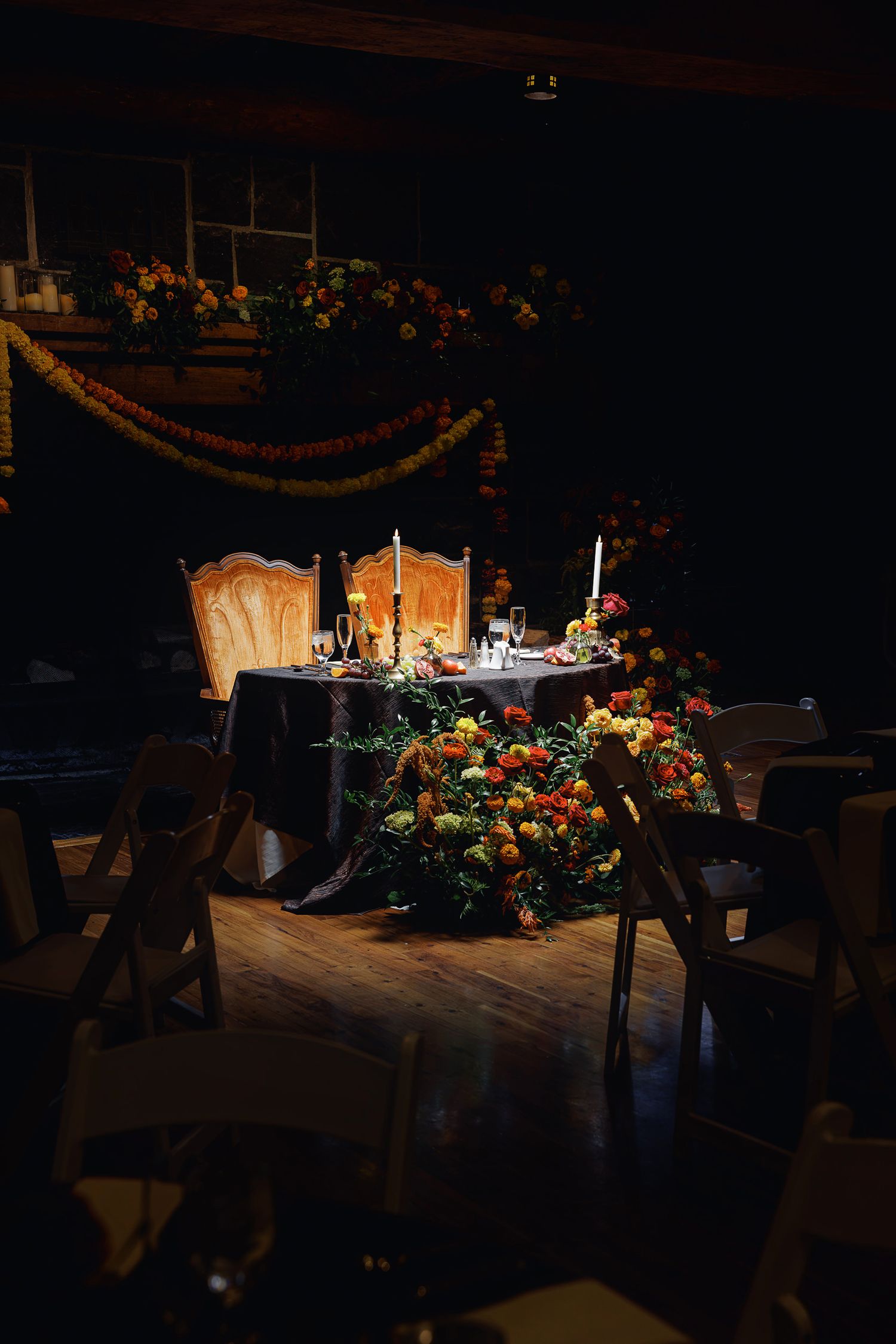 Romantic dimly lit sweetheart table adorned with colorful floral arrangements and candles for an elegant wedding reception.